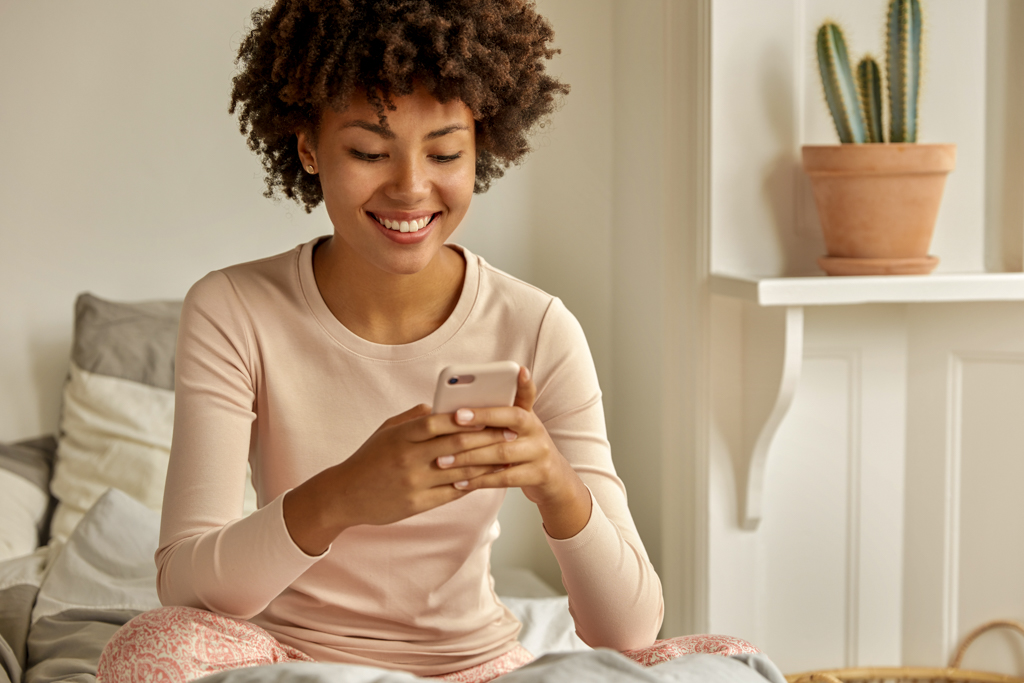 Frau sitzend auf dem Bett mit dem Handy