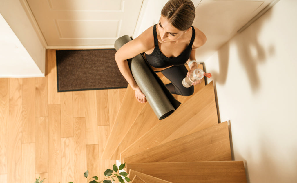 Frau läuft zuhause mit einer Yoga Matte die Treppe hoch, um Sport zu machen