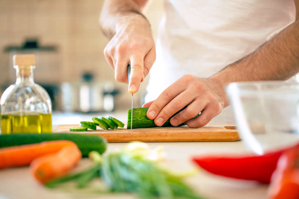 Hände von einem Mann der in der Küche steht und Gemüse schneidet