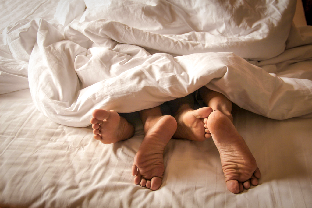 Unterseite der Füße von einem Paar im Bett und mit Bettdecke