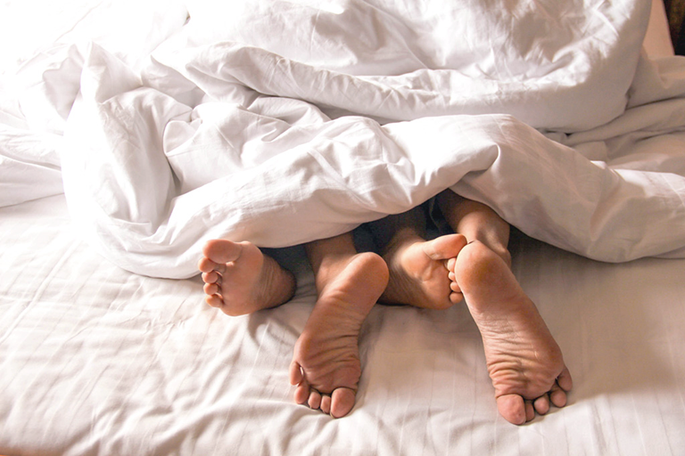 Füße von einem paar die unter der Bettdecke liegen